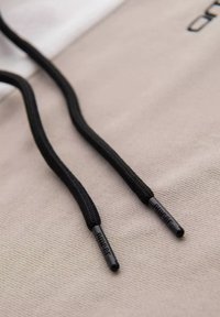 Cordones de zapato negros y texturizados con extremos metálicos que presentan una marca grabada, colocados sobre una superficie de tela beige clara.