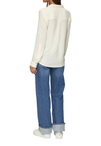 Weißes Langarmblusen mit Kragen und knöpfbaren Ärmeln, kombiniert mit blauen, weit geschnittenen Jeans und weißen Sneakers. Glatte Stofftextur.