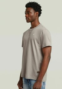 Camiseta de algodón gris con mangas cortas, cuello redondo y un pequeño logo en el pecho. Combinada con jeans de mezclilla azul.