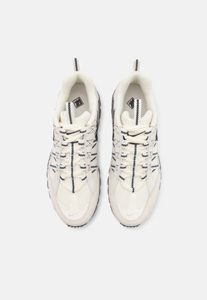 Bílé sportovní tenisky s texturovanou síťovinou a koženým svrškem, s černými akcenty a výrazným systémem šněrování na tmavé gumové podrážce.