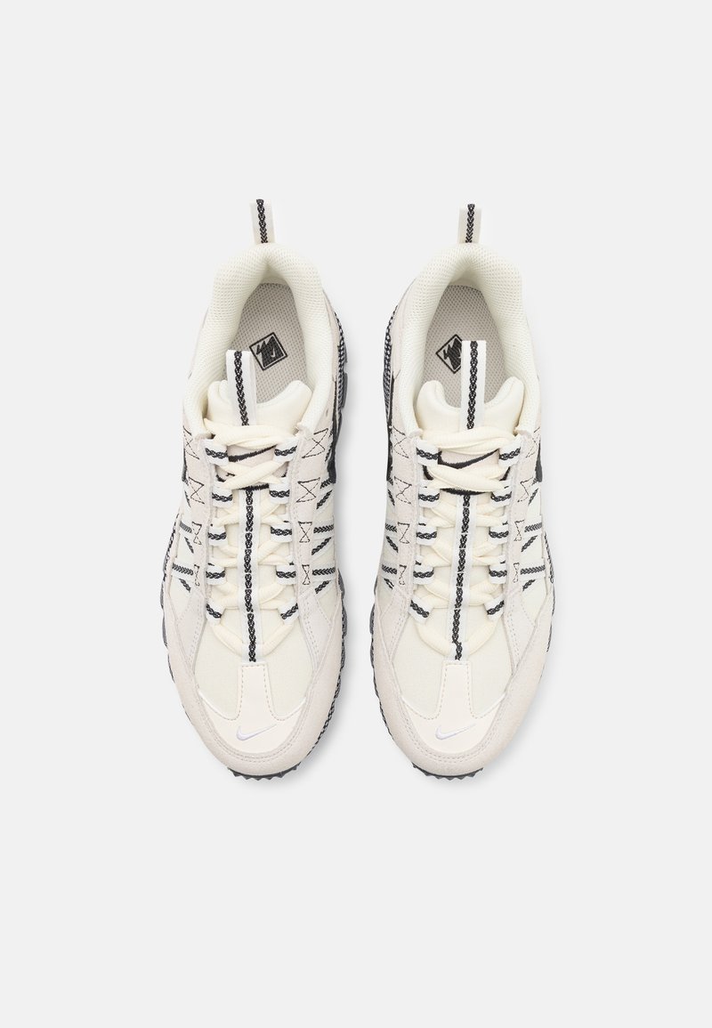 Baskets blanches sportives avec dessus en mesh texturé et cuir, comprenant des accents noirs et un système de laçage distinctif sur une semelle en caoutchouc foncé.