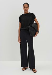 Haut noir texturé à manches courtes, coupe décontractée, associé à un pantalon noir ample et un sac tissé noir, des sandales plates complètent l'ensemble.