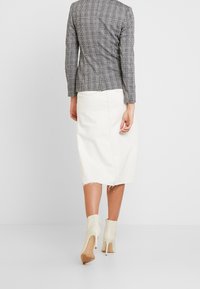 Grijs geruit blazer, witte dennenrok met rafelige zoom en lichtbeige enkellaarsjes met een slanke hak, gezien van achteren.