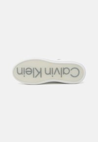 Calvin Klein sneaker sole, white rubber, rounded shape, clear bottom with gray logo, smooth texture, minimal design, no visible patterns.