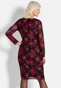 Schwarzes Kleid mit langen Ärmeln, mit einem Blumenmuster in Rot und Beige. Es hat eine figurbetonte Silhouette und einen Reißverschluss auf der Rückseite.