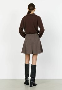 Suéter de punto marrón con cuello en punta, combinado con una falda de cuadro acampanada en tonos marrones. Botas altas de tacón negro completan el atuendo.