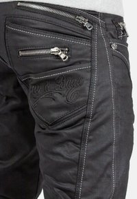 Jean en denim noir avec plusieurs poches zippées, couture blanche contrastante et détails de logo brodés sur la poche arrière.