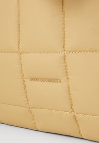 Quilted beige handbag with a smooth, padded texture. Features embossed logo and contrasting stitching detail. Rectangular shape.