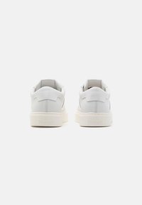 Sneaker in pelle bianca con profilo basso, punta rotonda e tacco imbottito. Presentano una suola in gomma bianca testurizzata e un marchio discreto.