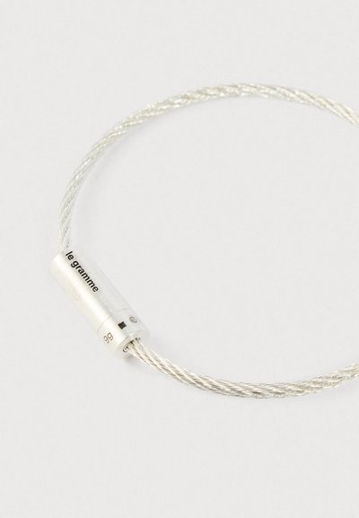 Sudraba savītā vadu aproce ar cilindrisku aizdari, kurā iegravēts "le gramme" un "9g" uz vienkārša balta fona.