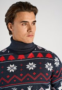 Mörkblå polotröja med festliga mönster i rött och vitt, inklusive snöflingor, träd och renar. Mjuk stickad textur.