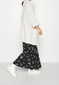 Cardigan lavorato a maglia spesso di colore crema, gonna maxi nera a fiori con fiori multicolori, e sneakers bianche con suola testurizzata.