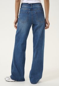 Jean large en denim bleu foncé, avec une taille haute, deux poches arrière et une finition propre au niveau de l'ourlet, associés à des baskets blanches.