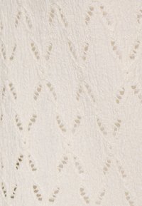 Biały materiał z fakturowanym wzorem zygzakowym i wycięciami. Tkanina wydaje się lekka i przewiewna.