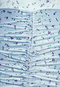 Ljusblå ärmlös klänning med små lila blommönster. Har en samlad textur längs det centrala sömmen, vilket skapar en figurnära silhuett.