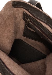 Intérieur d'un sac en cuir brun foncé avec un doublure en suède beige douce ; présente de petites poches zippées et une base structurée pour l'organisation.