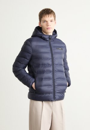 Giacca imbottita blu navy con cappuccio, design a righe orizzontali, chiusura con zip e patch del logo sul davanti. Tessuto morbido e vestibilità rilassata.