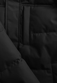 Zwarte gewatteerde jashulz met een gladde textuur, twee verticale zakken en doorstikte naden op het oppervlak.