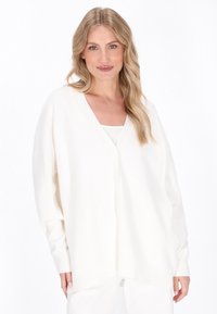 Weißer Cardigan mit V-Ausschnitt, Knopfverschluss und langen Ärmeln. Aus weichem Stoff mit einem lockeren, oversized Schnitt.