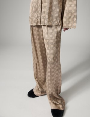 Pantalon ample beige à motifs et haut à manches longues assorti, porté avec des chaussons noirs duveteux, présenté sur une personne debout devant un fond gris.