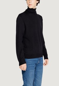 Maglione a collo alto nero con tessuto texturizzato, maniche lunghe e polsini e orlo a costine, abbinato a jeans azzurri chiari.