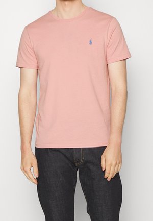 Lichtroze katoenen t-shirt met een ronde hals. Heeft korte mouwen en een klein blauw logo op de borst. Eenvoudig en klassiek ontwerp.