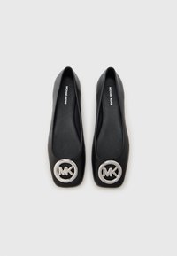 Μαύρα δερμάτινα μπαλαρίνια με τετράγωνη μύτη και ένα έντονο ασημί λογότυπο MK στη μύτη. Λεπτή υφή και casual σχεδιασμός.