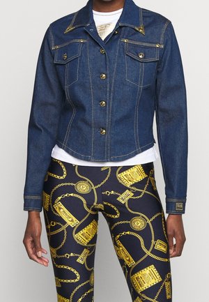 Dunkelblaue Jeansjacke mit goldenen Knöpfen und Nähten, kombiniert mit schwarzen Leggings mit goldenen Ketten- und Anhängermustern.