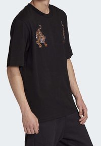 Svart t-shirt med kort ärm som har livfulla broderade tigerdesigns i orange och vitt på framsidan. Mjuk i bomullsmaterial.