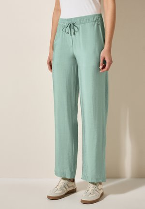 Pantalons larges vert clair en matériau doux avec une taille élastique et un cordon de serrage. Présentent une texture lisse et des coutures latérales.