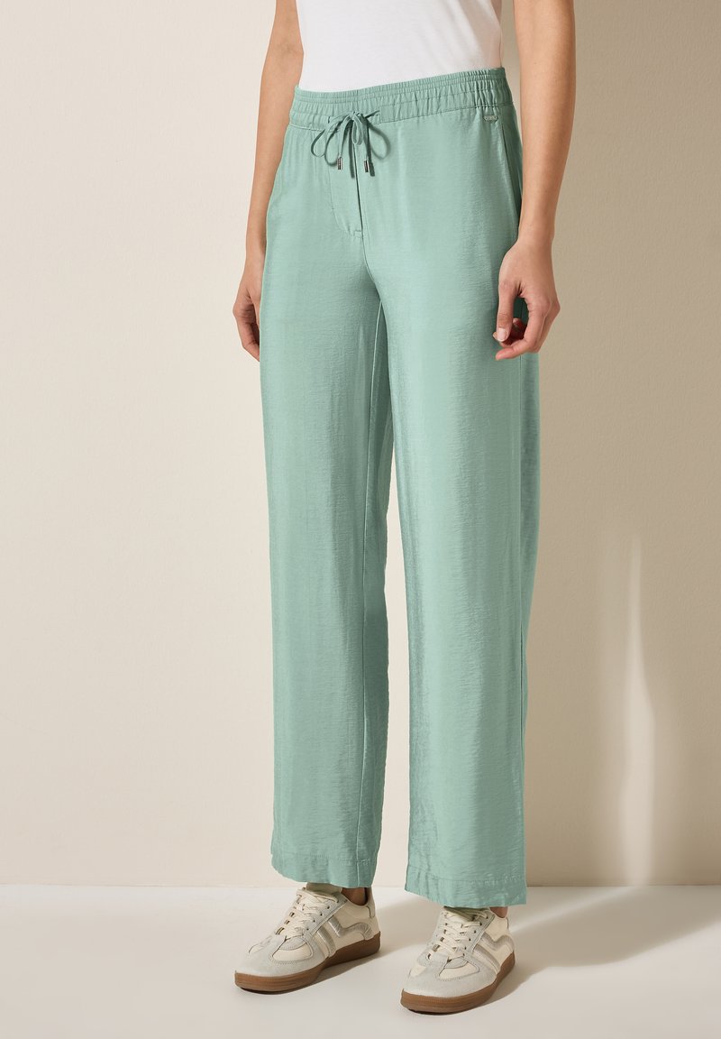 Pantalons larges vert clair en matériau doux avec une taille élastique et un cordon de serrage. Présentent une texture lisse et des coutures latérales.
