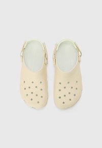 Lyse beige klomper med ventilasjonsåpninger, justerbare stropper og en glatt, gummilignende tekstur. Designet for komfort og pusteevne.