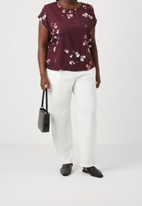 Bordeaux bloemenblouse met korte mouwen, gecombineerd met witte wijde broek. Zwarte gestructureerde handtas en zwarte geweven instap schoenen.