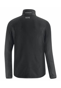 Chaqueta negra con cuello alto, mangas largas y adornos reflectantes. Presenta una textura suave y el logo de GORE en la parte superior de la espalda.