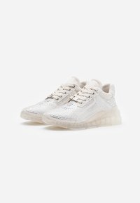 Chaussures de sport blanches avec une surface en cristal scintillant, un tissu texturé et une semelle épaisse translucide. Lacets et œillets en métal visibles.