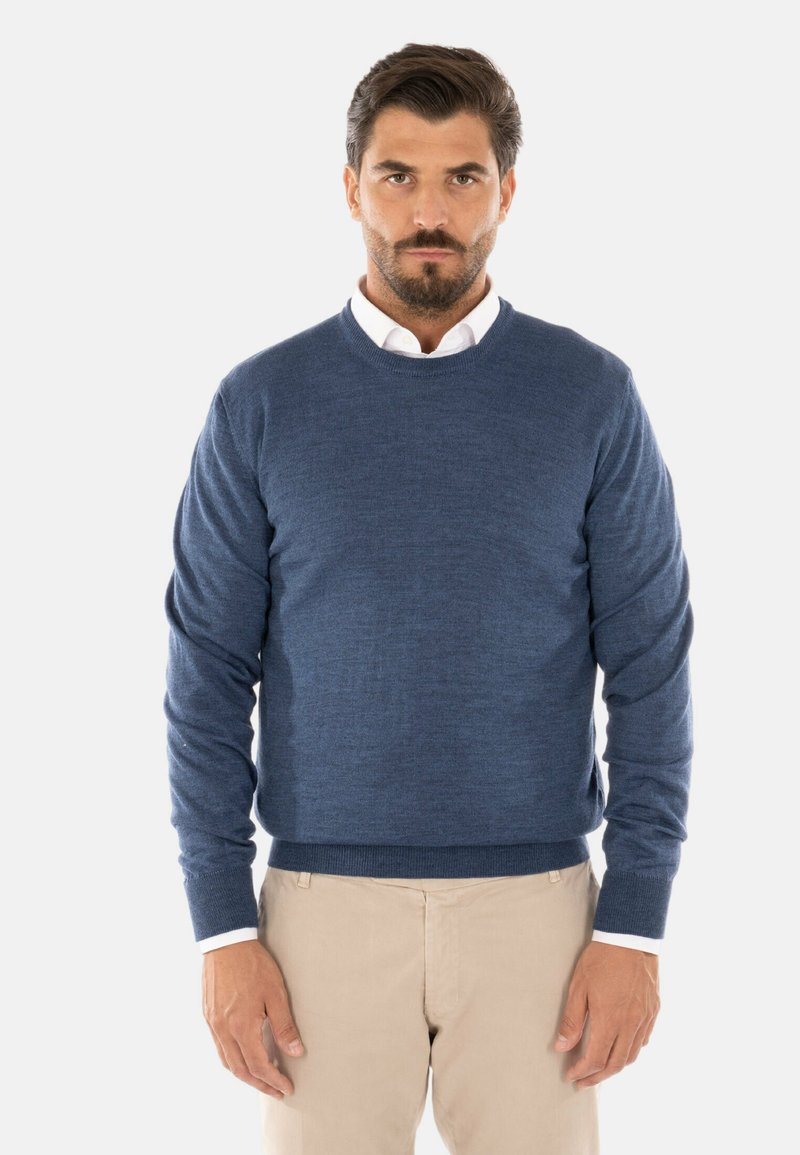 Maglione blu da uomo con collo rotondo, realizzato in morbido tessuto a maglia, con polsini e orlo a costine, indossato sopra una camicia bianca con colletto.