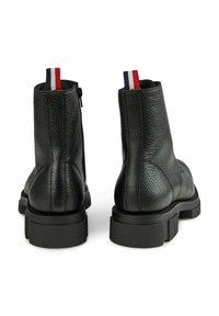 Zwarte leren enkellaarsjes met een gestructureerd oppervlak, met een zwarte rubberen zool en een rood, wit en blauw trekbandje voor eenvoudig aan- en uittrekken.