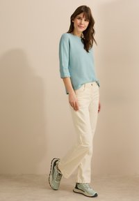 Ljusblå texturerad tröja med trekvartsärmar, ihop med krämfärgade byxor och ljusgröna träningsskor.