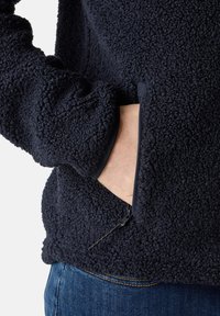 Giacca in pile blu navy con una texture morbida, dotata di una tasca laterale con zip e un design delle maniche aderente.