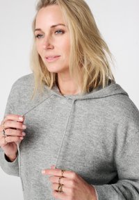 Grijze capuchontrui met een zachte textuur en een losse pasvorm. Voorzien van trekkoorden, lange mouwen en subtiele naaddetails.