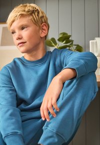 Plava flis majica i hlače u kompletu, mekana tekstura, opušteni kroj, rebrasti rukavi i dizajn s okruglim izrezom. Ležerna, udobna odjeća.