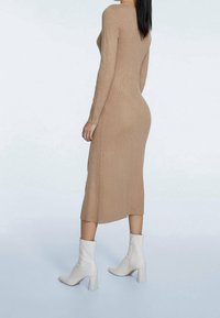 Abito a maglia beige a costine, con maniche lunghe e silhouette aderente, dotato di spacchi laterali, abbinato a stivaletti bianchi alla caviglia con tacco a blocco.