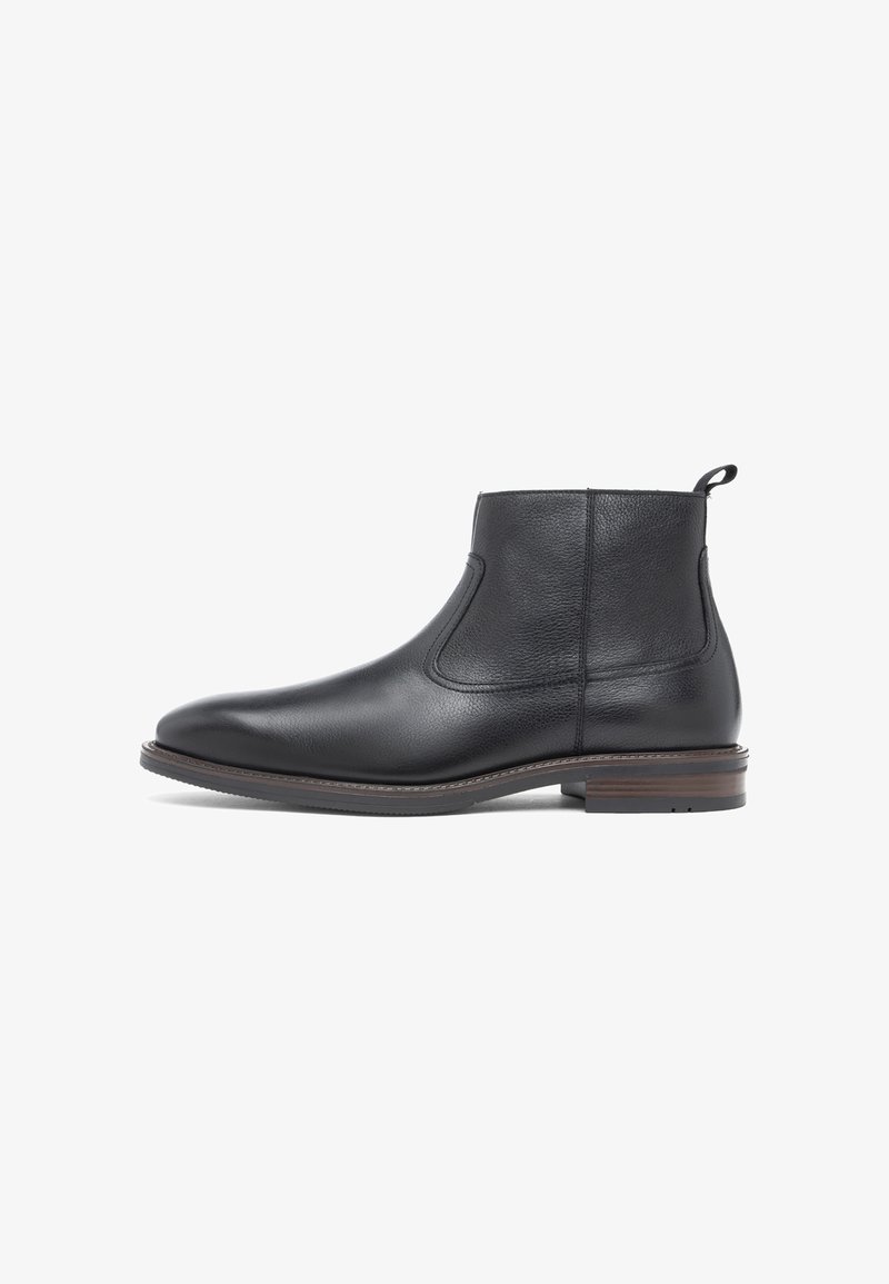 Bottine en cuir noir avec bout arrondi, languette au talon et semelle basse en bois empilée sur fond blanc.