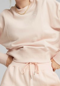 Felpa rosa con collo alto e polsini a coste, con un piccolo dettaglio logo, abbinata a pantaloni tuta coordinati con coulisse.