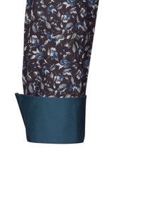 Polsino con tessuto a fantasia floreale blu scuro e bordo del polso verde turchese ribaltato su sfondo bianco.