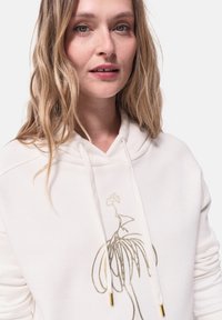Weißer Kapuzenpullover mit Kordelzug, der eine goldene, liniengezeichnete Grafik einer Pflanze zeigt. Weiche Textur, lässiges Design, mit metallischen Akzenten an den Kordelzugspitzen.