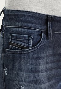 Jeans de denim en azul oscuro con una textura desgastada, que presentan un pequeño bolsillo trasero y un sutil desgaste en la tela.