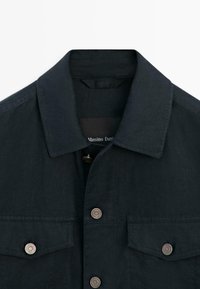 Veste bleu marine foncé à boutons, avec un col et deux poches poitrine avec des boutons ronds en métal.