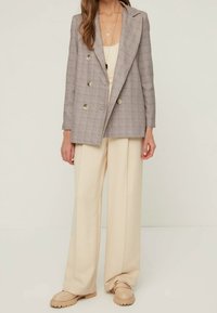 Blazer doppiopetto in tessuto a quadri grigio chiaro, con grandi bottoni e rever a punta, abbinato a pantaloni beige a gamba larga.