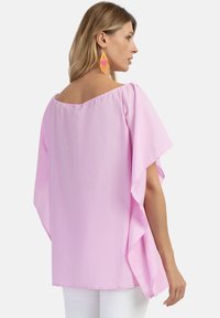 Lyserød, let bluse med flagermusærmer, scoop-halsudskæring og en flydende design. Parret med farverige perleøreringe.